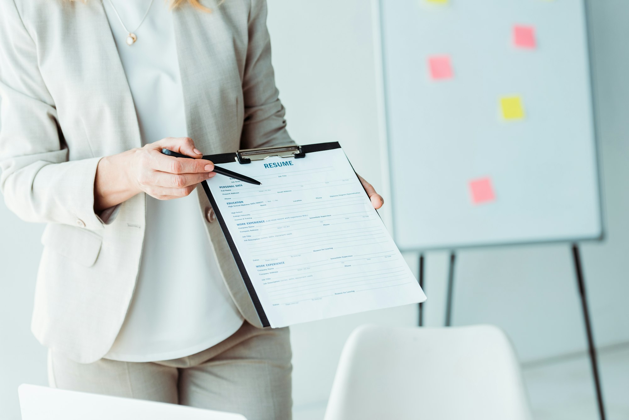 cropped view of woman holding clipboard with resume lettering and pen